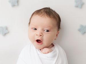 Alert newborn with wide eyes lying on white backdrop with blue star decorations in the background.