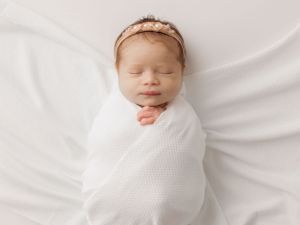 Serene newborn portrait with sparkly headband wrapped in soft white fabric.