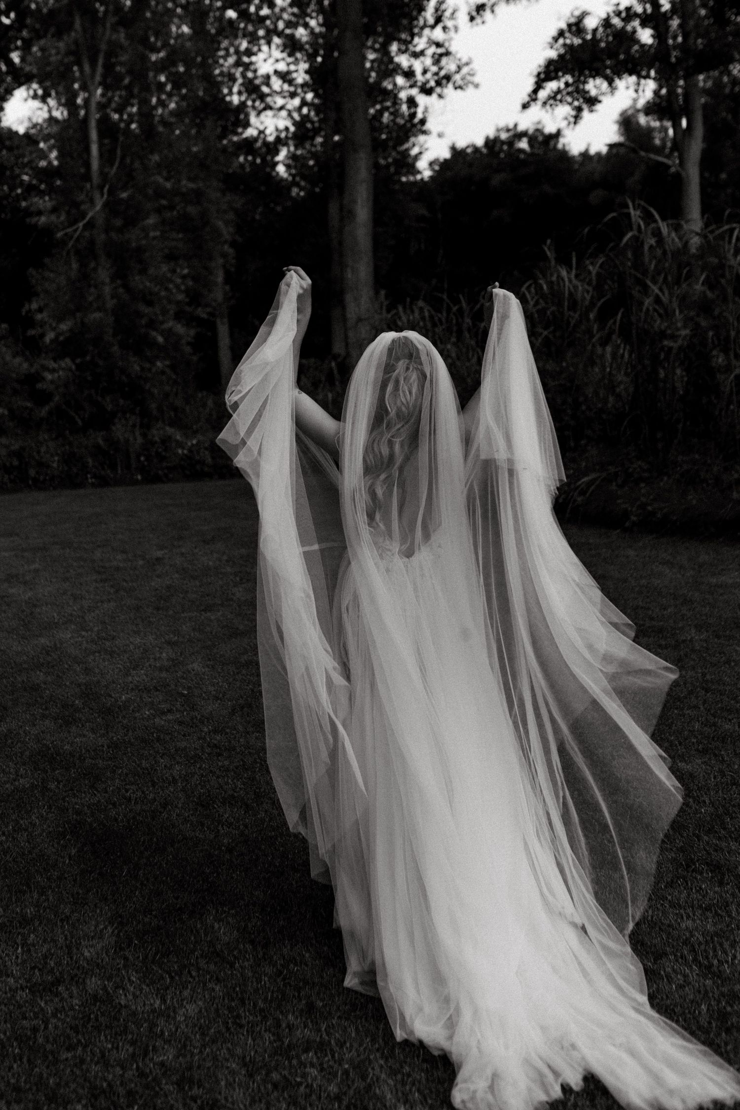 Dramatic black and white photo of bride's dress and veil flowing in outdoor garden setting.