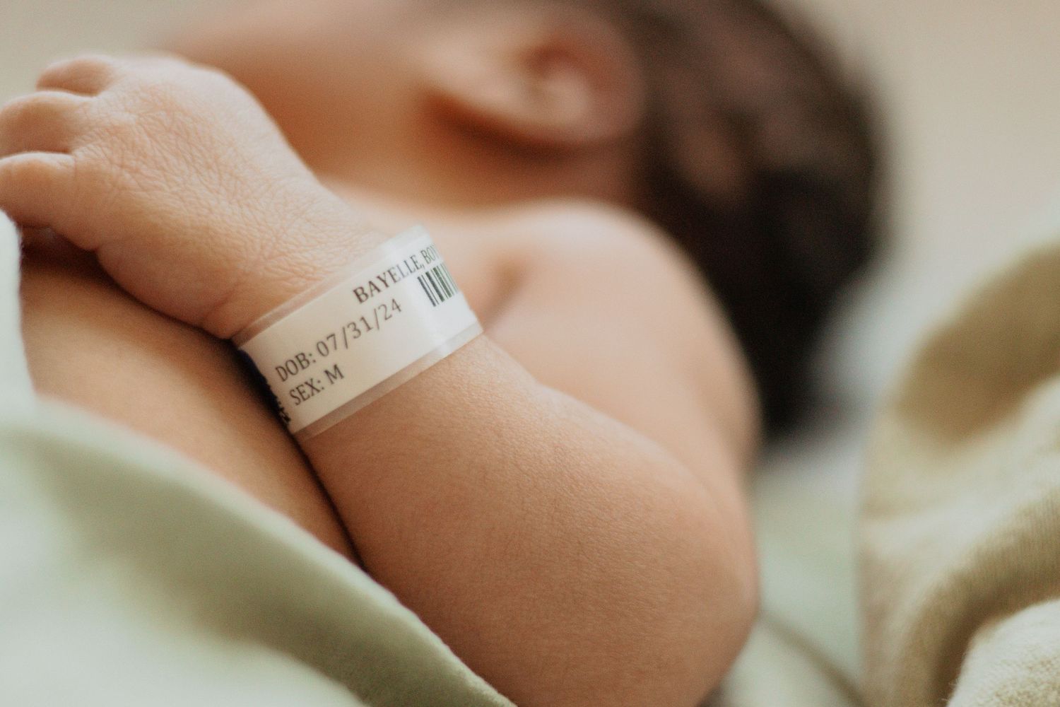 Close-up of a hospital ID bracelet on a newborn baby's arm against white bedding.