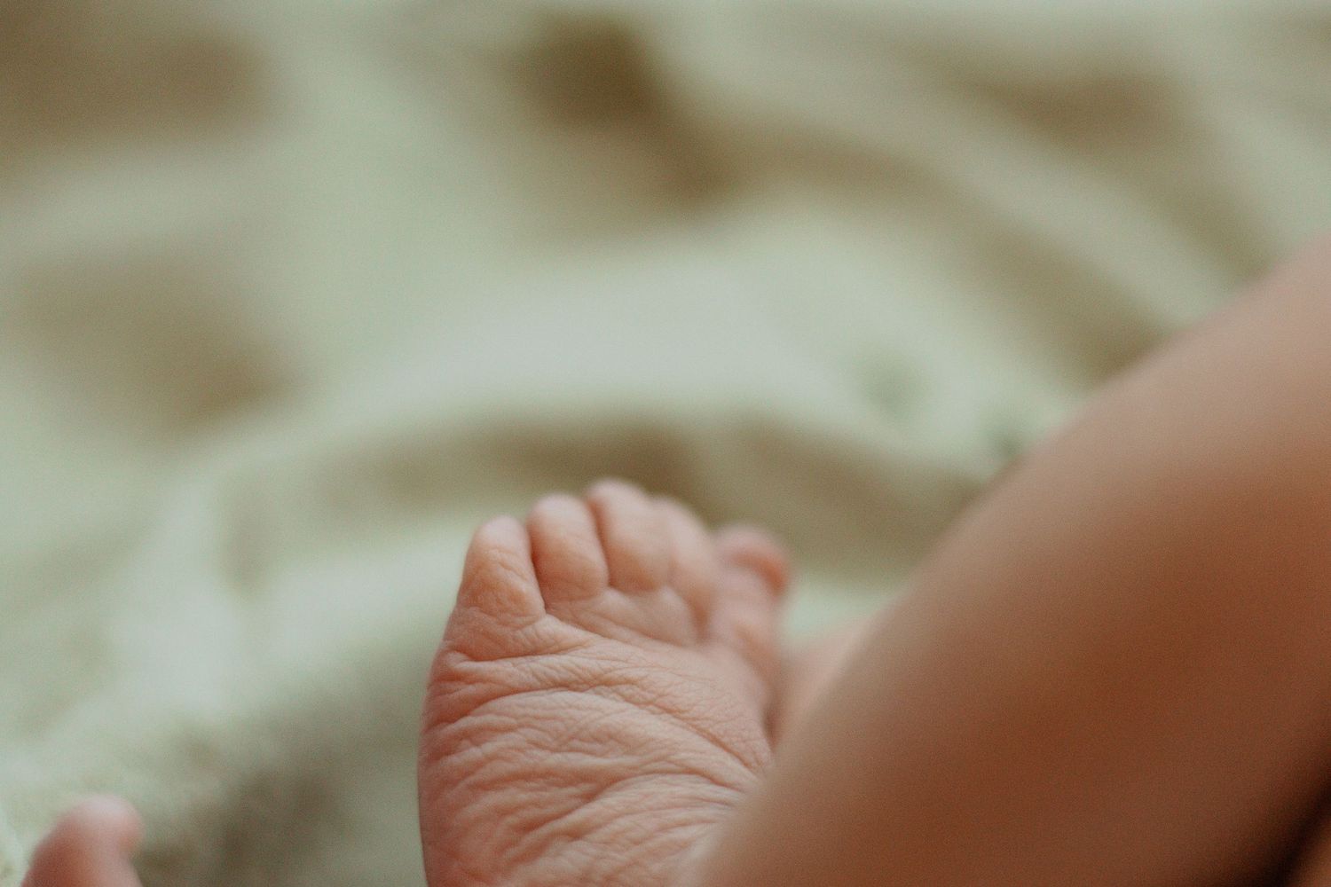 Macro shot of a newborn baby's tiny foot resting on soft beige fabric.
