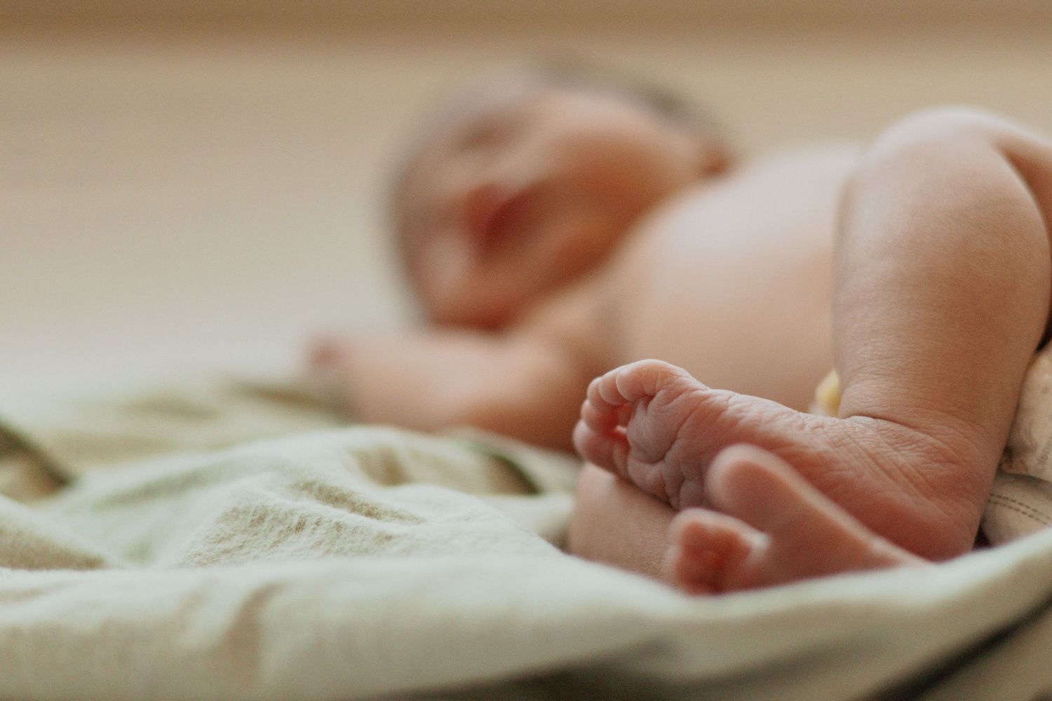 Newborn baby's feet and legs resting on light green hospital bedding.