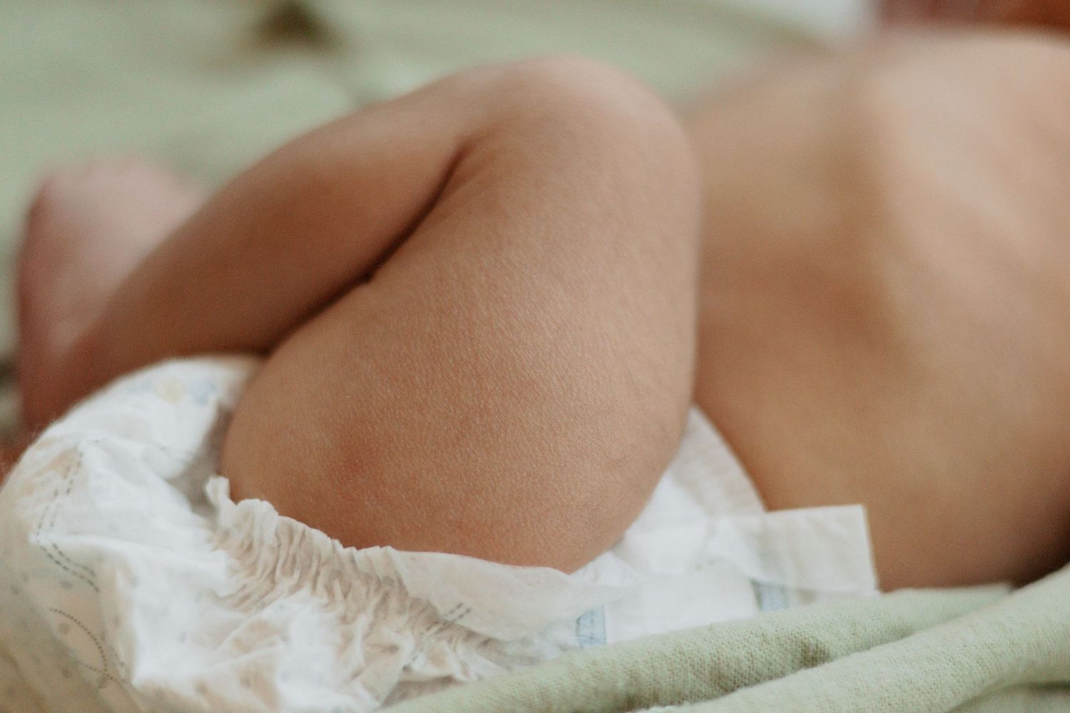Close-up of a newborn baby wearing a white diaper on mint green fabric.