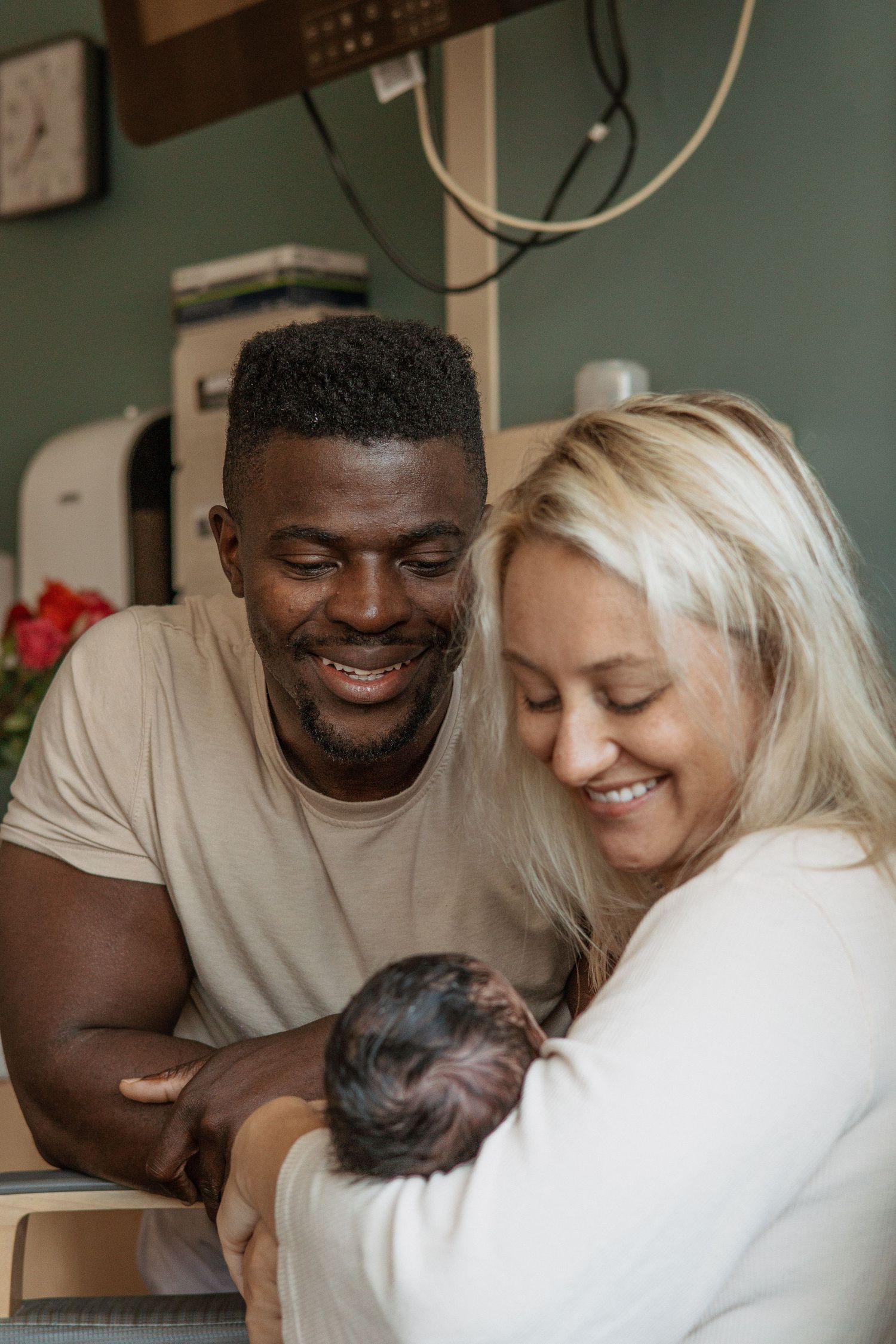 Happy parents smiling while holding their newborn baby in hospital room.