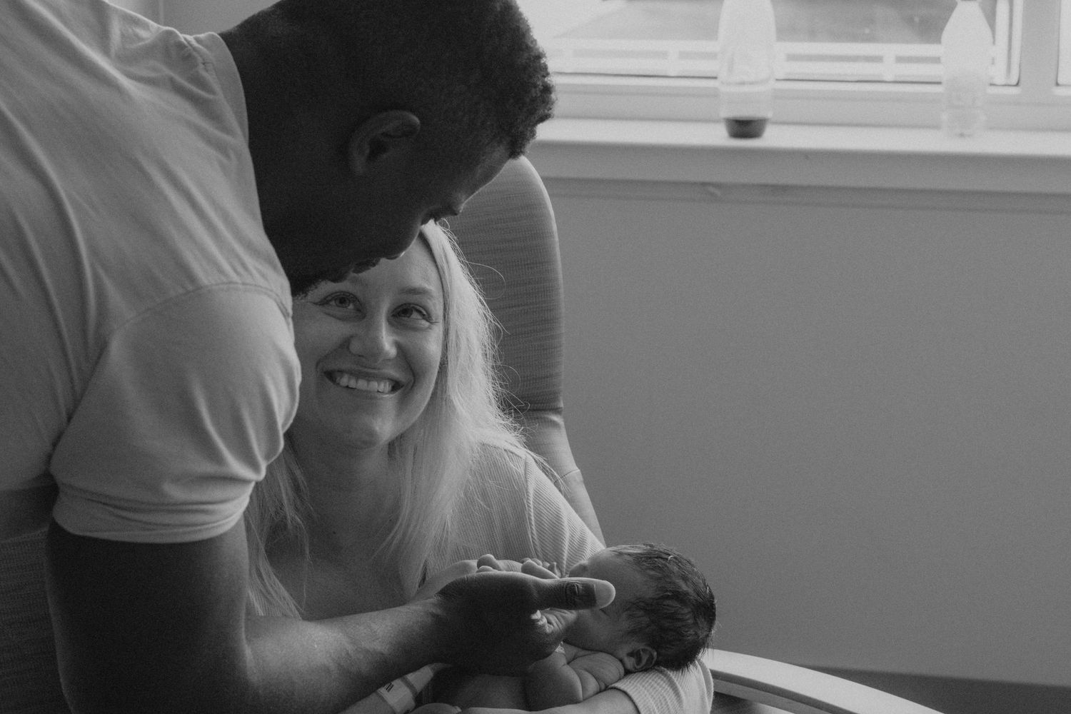 Black and white photo of new parents admiring their baby in hospital.