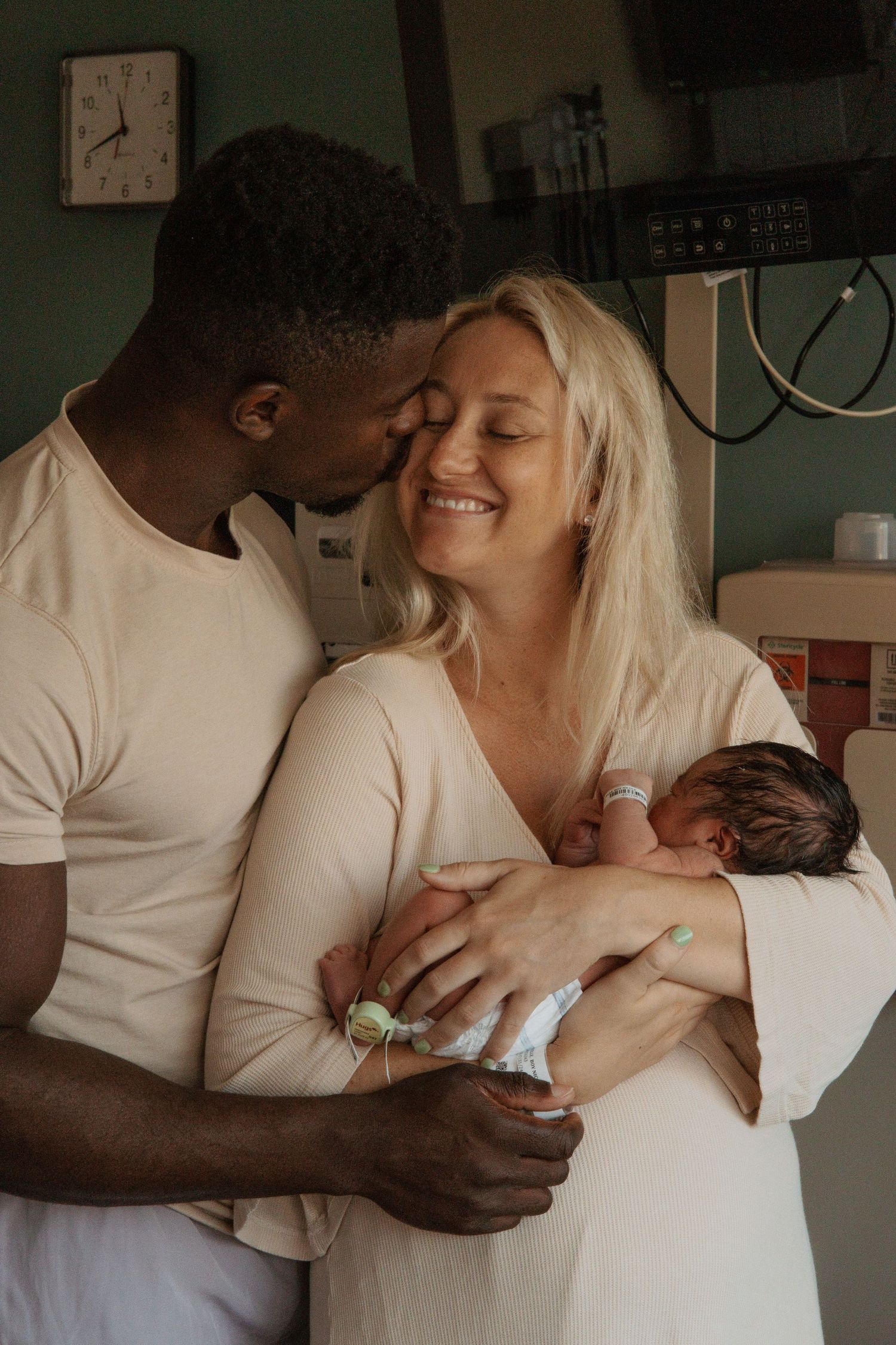 A loving family embrace as they hold their newborn in a hospital room.