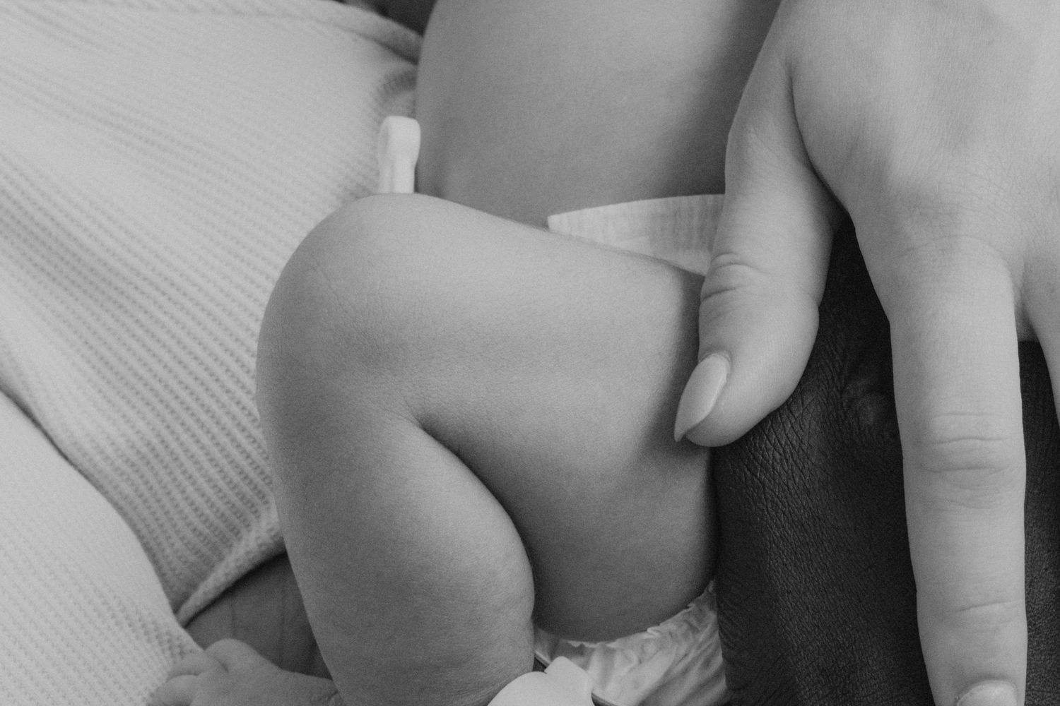 Close up black and white detail of tiny baby fingers touching soft fabric.
