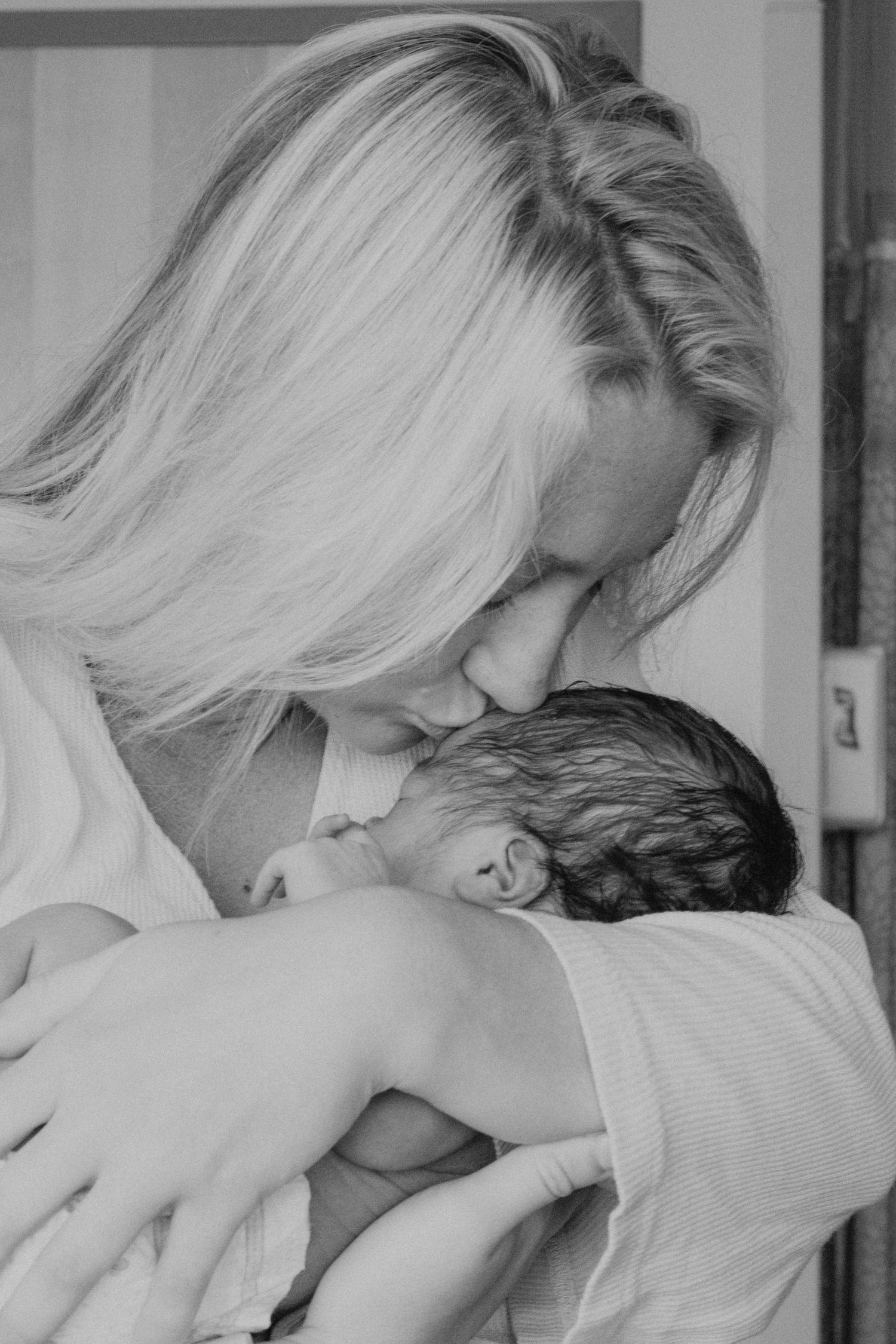 Intimate black and white portrait of parent kissing newborn baby's head.