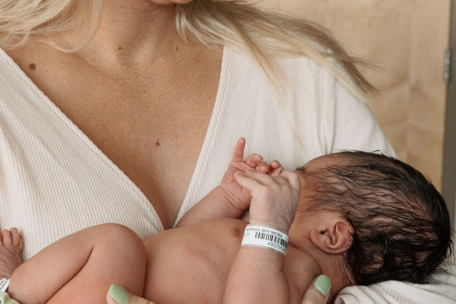 Newborn baby resting against parent wearing white in natural light setting.