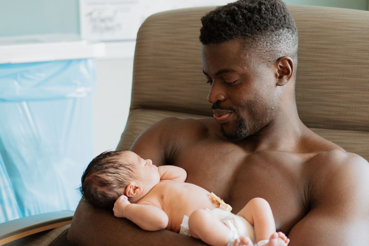 Parent gently cradling sleeping newborn baby while resting in comfortable chair.