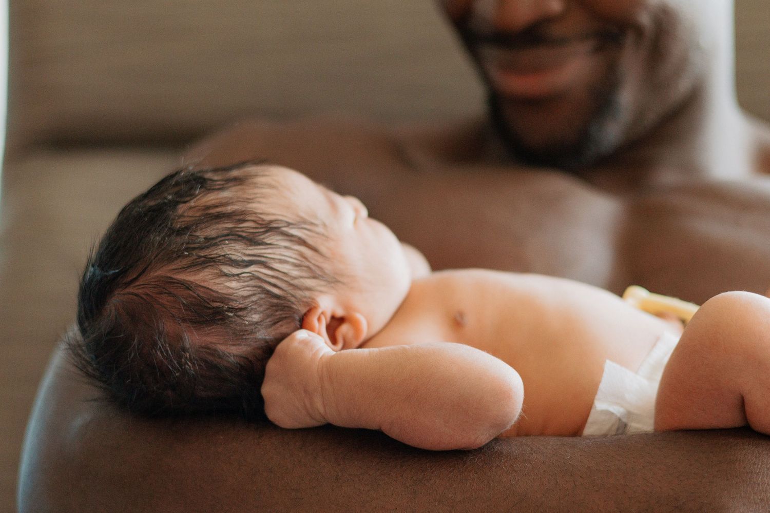 A tiny newborn infant rests on a caregiver's chest in an intimate bonding moment.