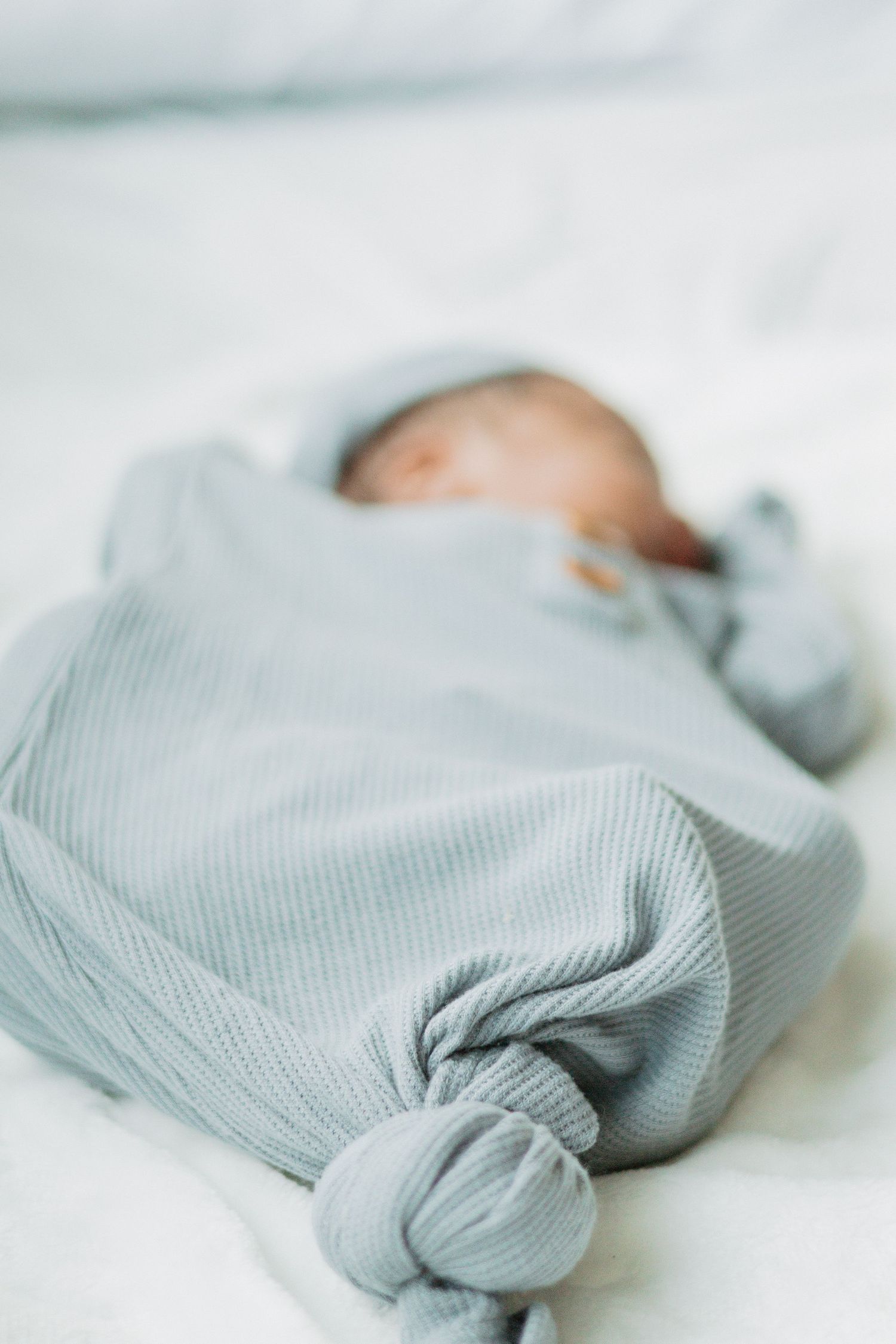 A swaddled newborn baby in soft grey clothing rests on white bedding.