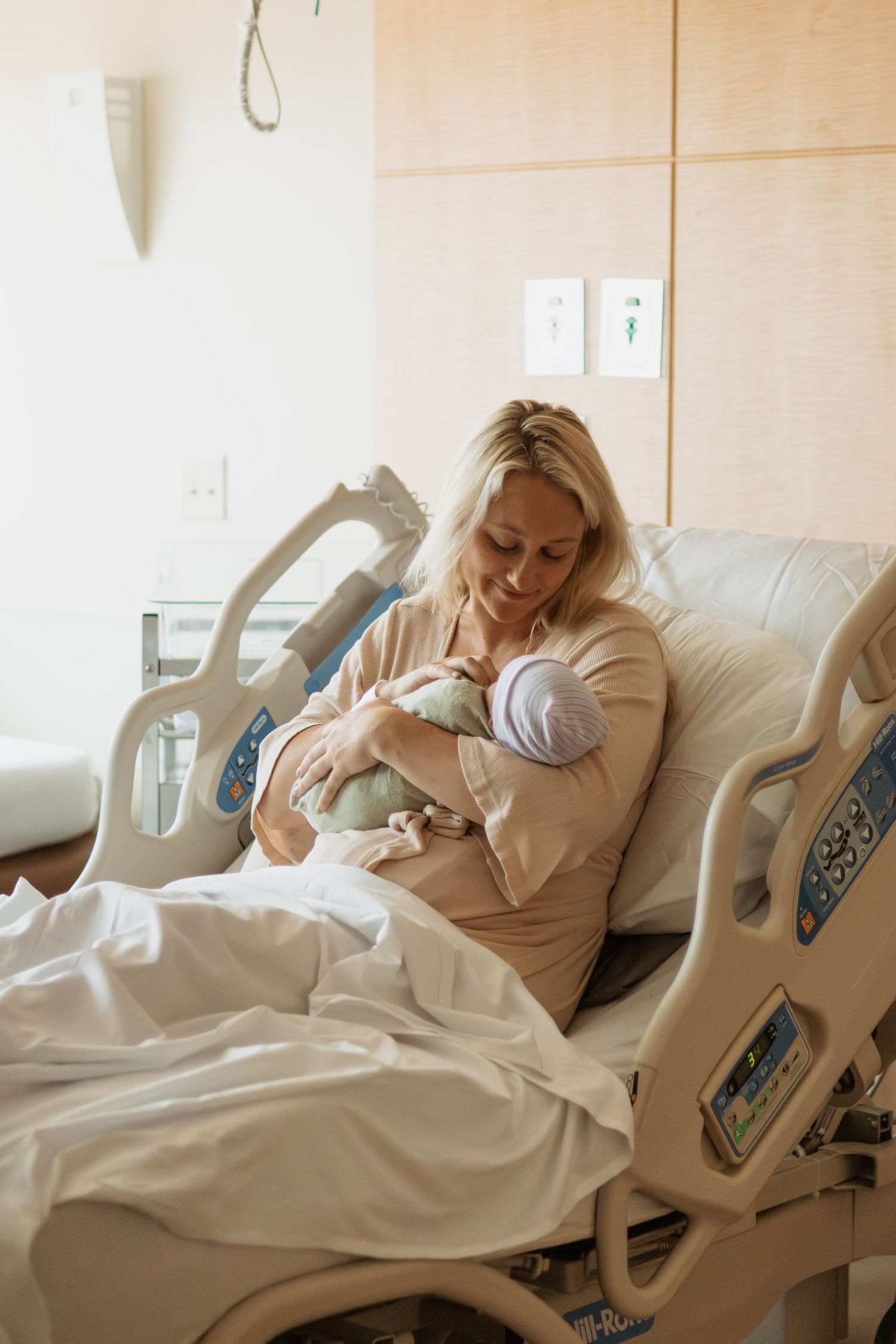 Parent tenderly holds newborn while resting in adjustable hospital bed.