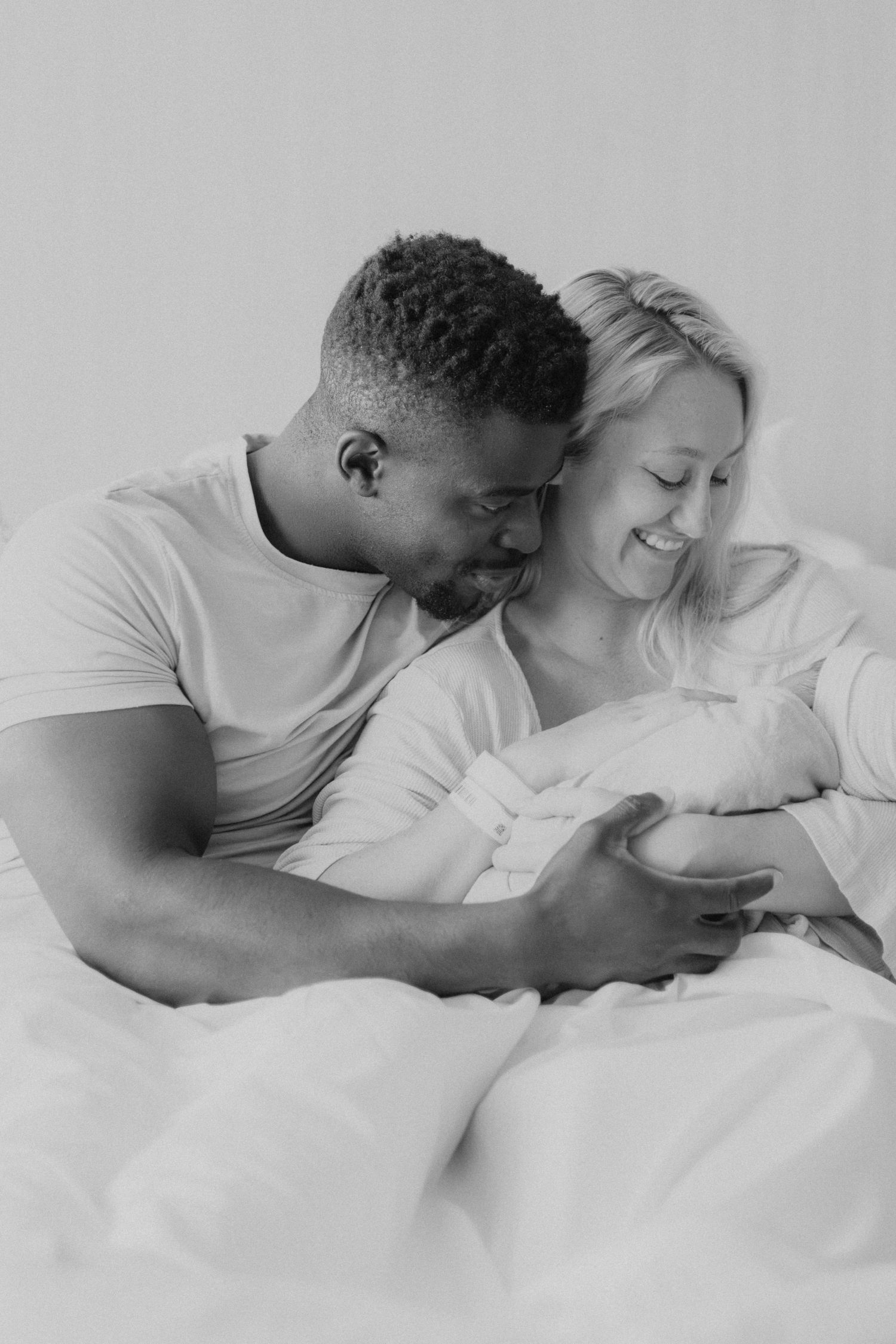 Intimate black and white portrait of new parents gazing at their newborn baby.