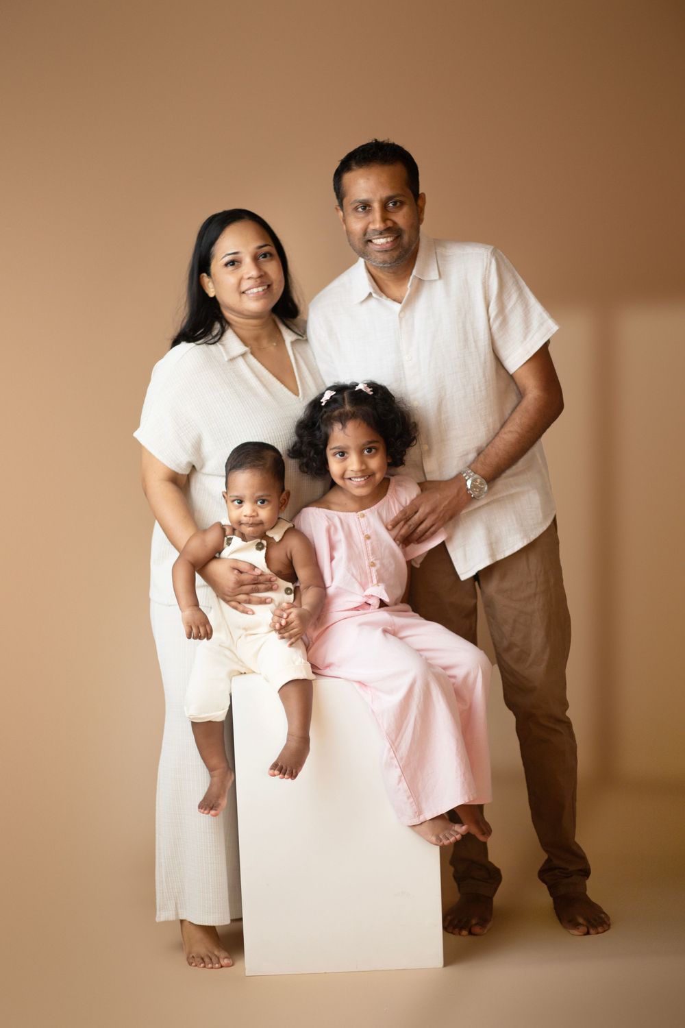 Studio portrait with children seated on white block against warm brown background.