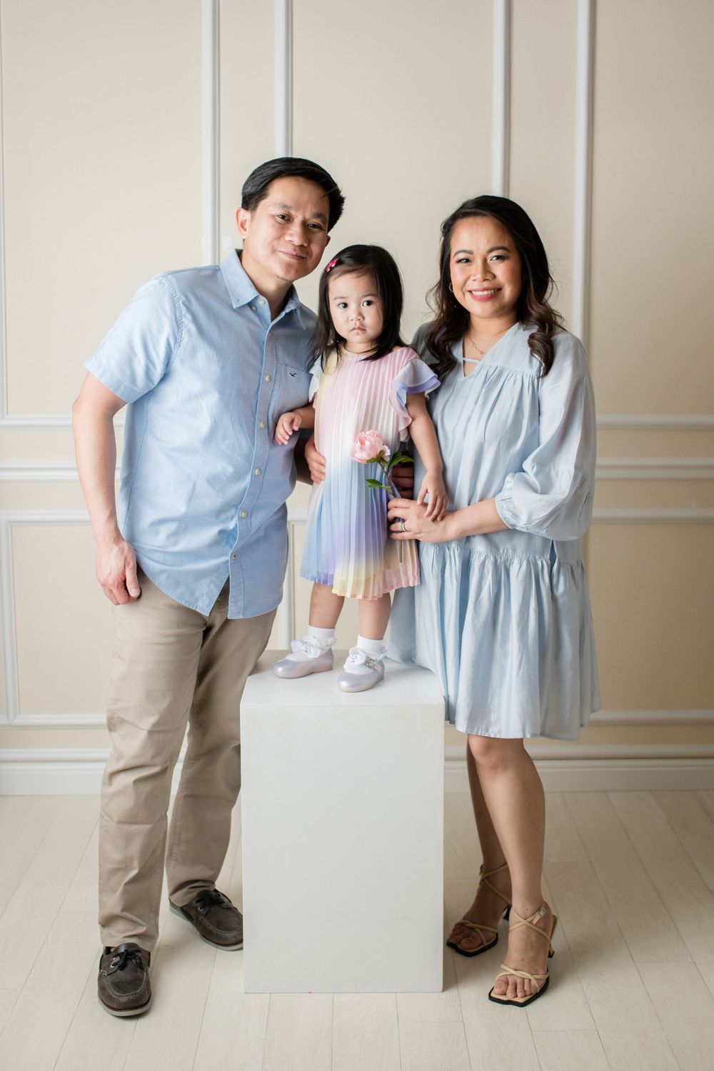 Studio portrait with child standing on white pedestal in pastel dress.