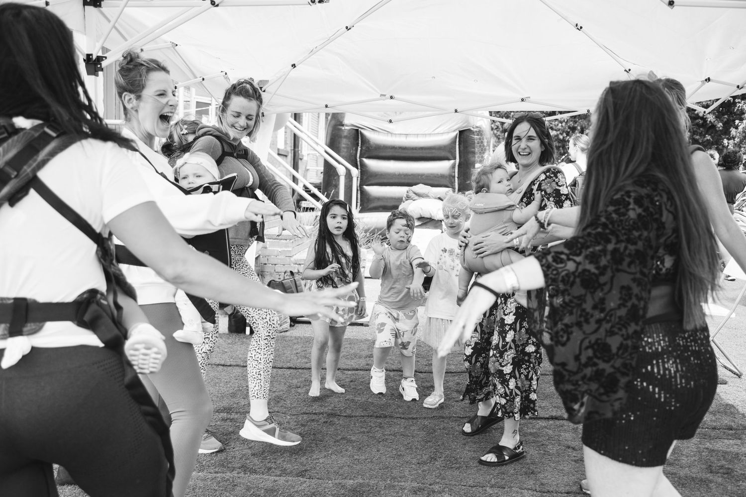 A group dances together at an outdoor event under white tents.