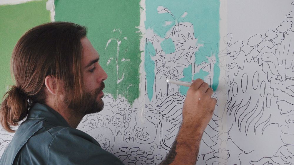 Artist drawing detailed line art on mint green wall mural.