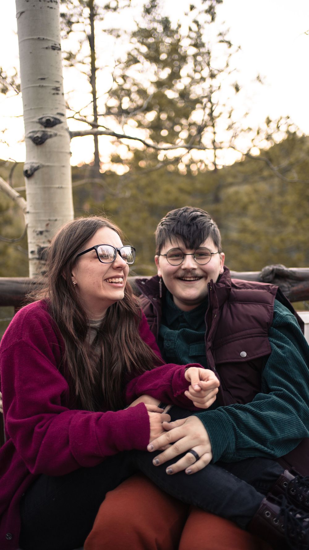 Two people sharing laughter while sitting together outdoors near a birch tree.