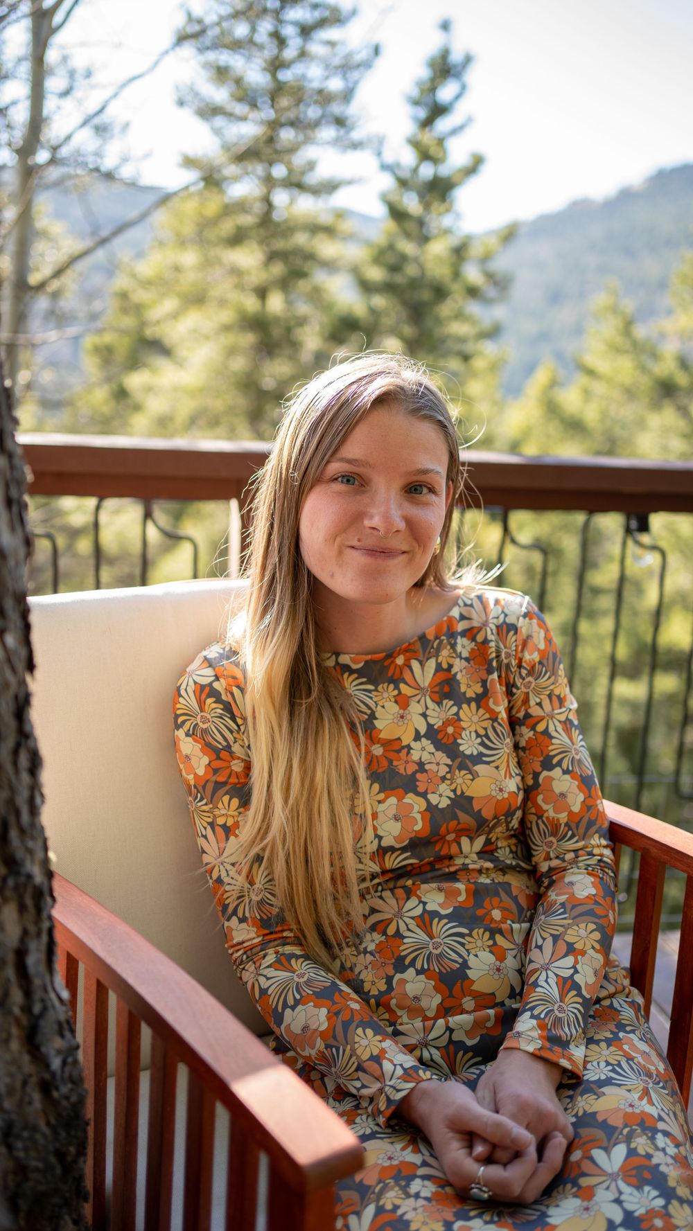 Person in floral dress sitting on mountain deck with scenic forest view.