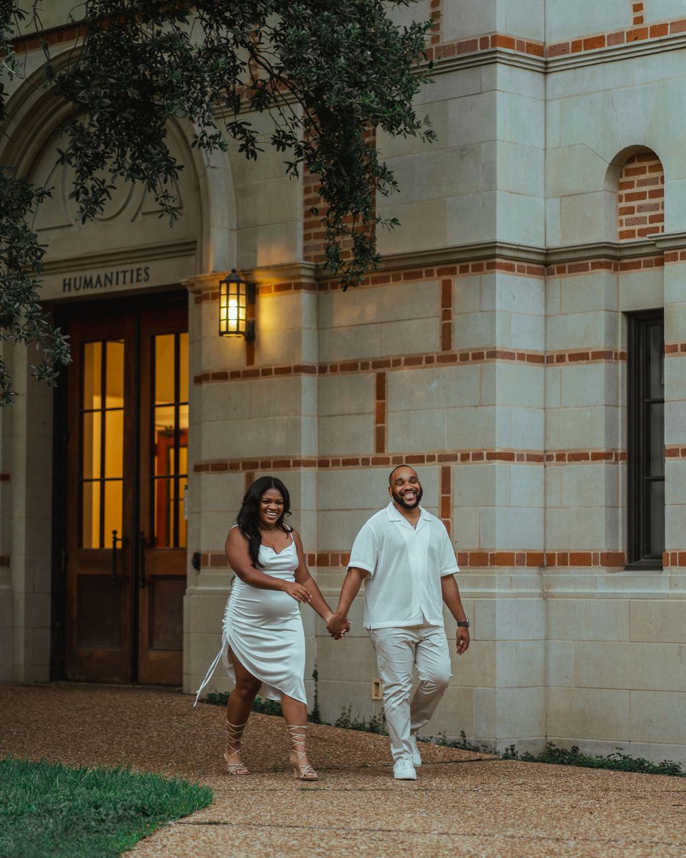 Couple walking hand in hand outside elegant stone building at dusk.