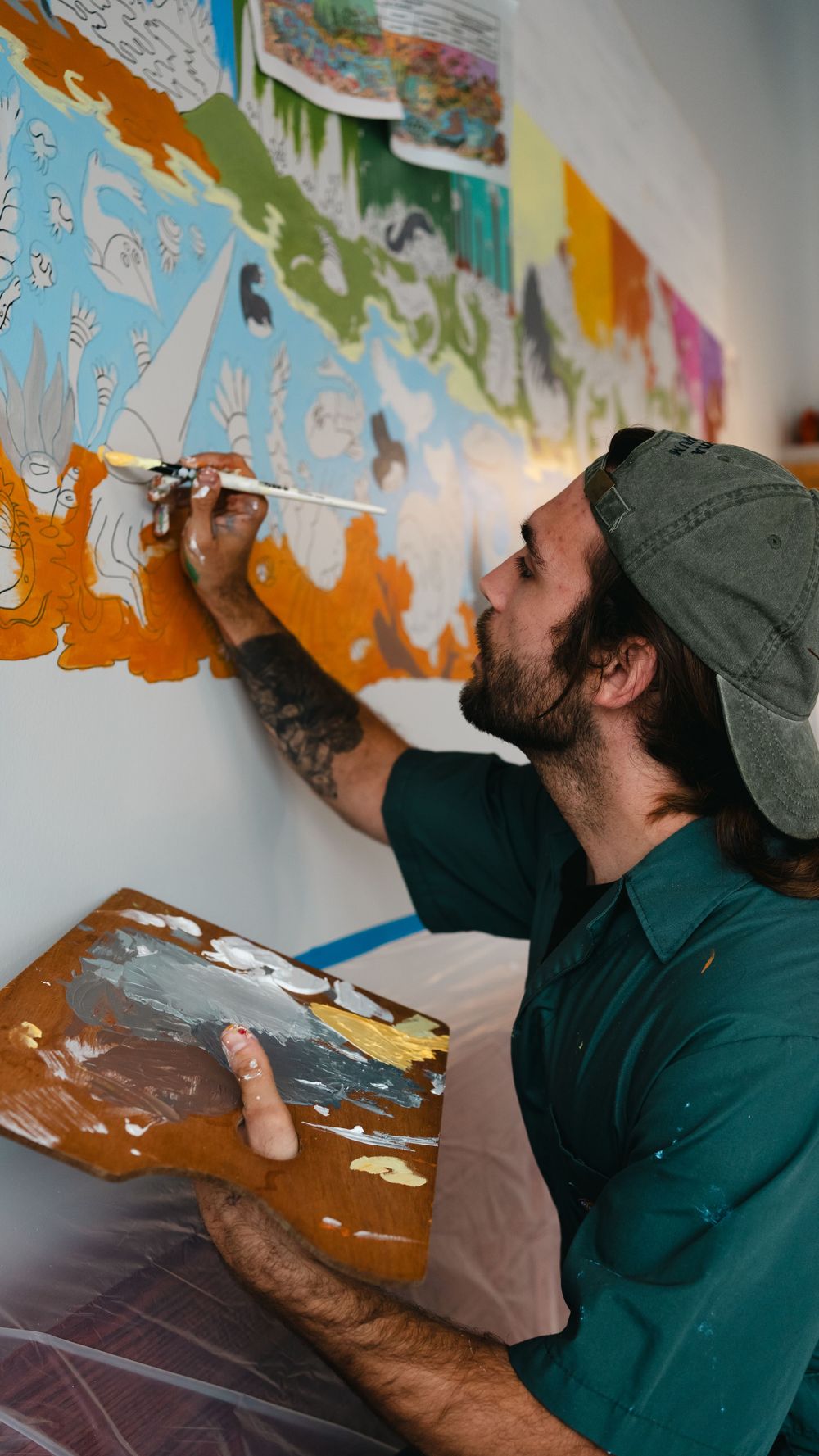 Artist holding paint palette while working on detailed colorful wall mural.