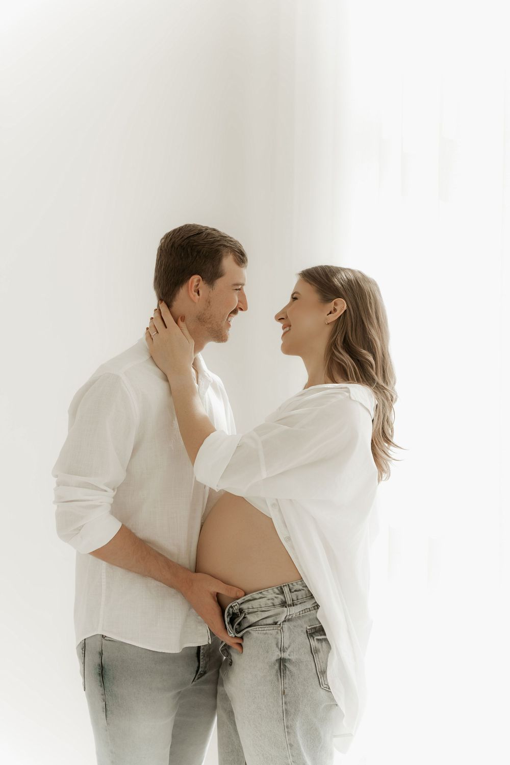 Romantic couple in white clothing embracing and laughing together in a minimalist white studio setting.