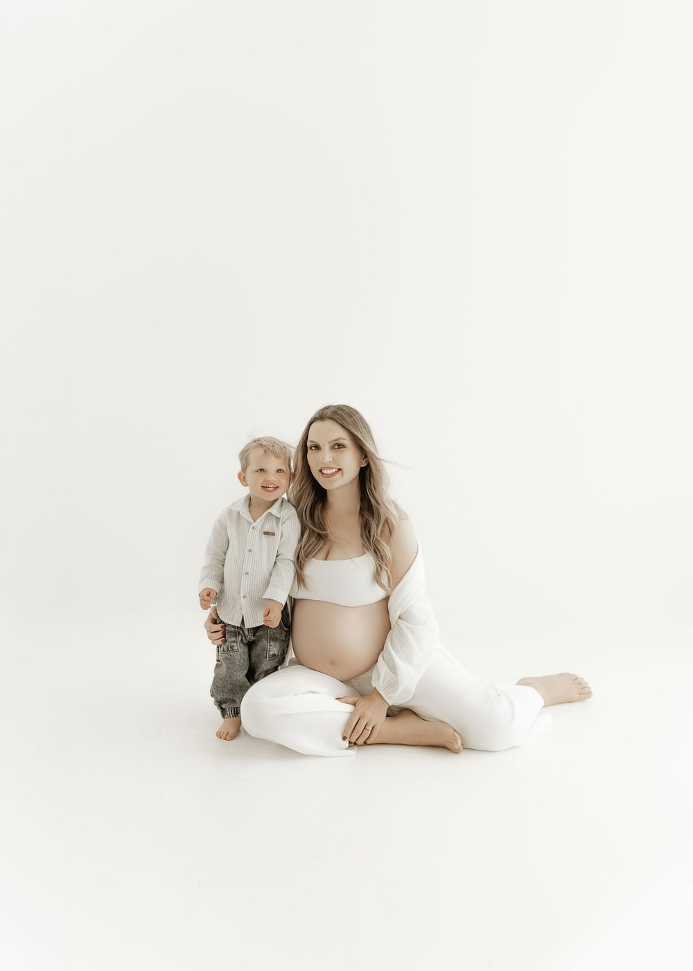 Minimalist maternity photography with soft white tones and gentle poses on a light backdrop.