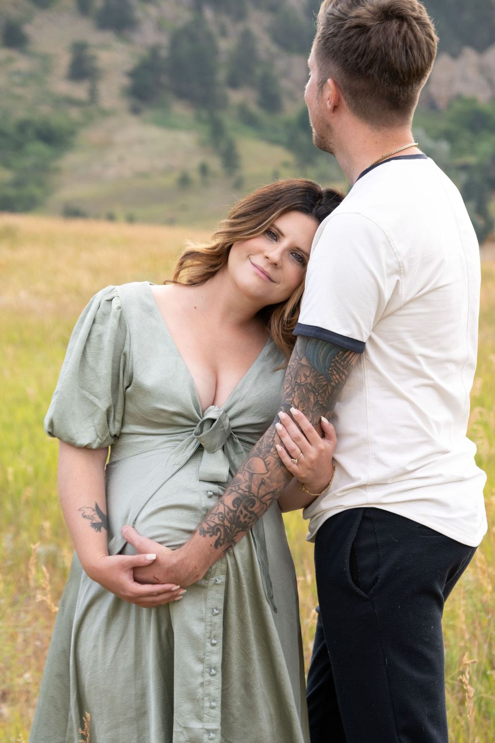 A tender moment between a couple wearing white and sage green in front of mountain scenery.