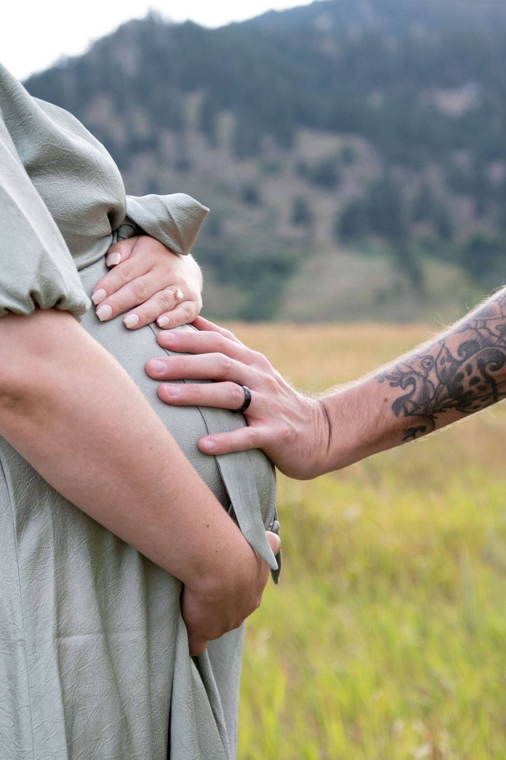 Close-up details of gentle hand holding against a soft sage green dress.