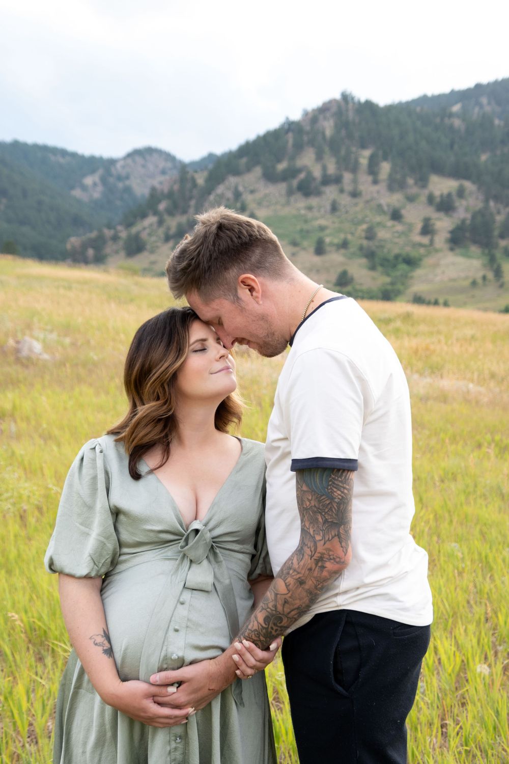 A romantic couple shares an intimate moment in a field with mountains in the background.