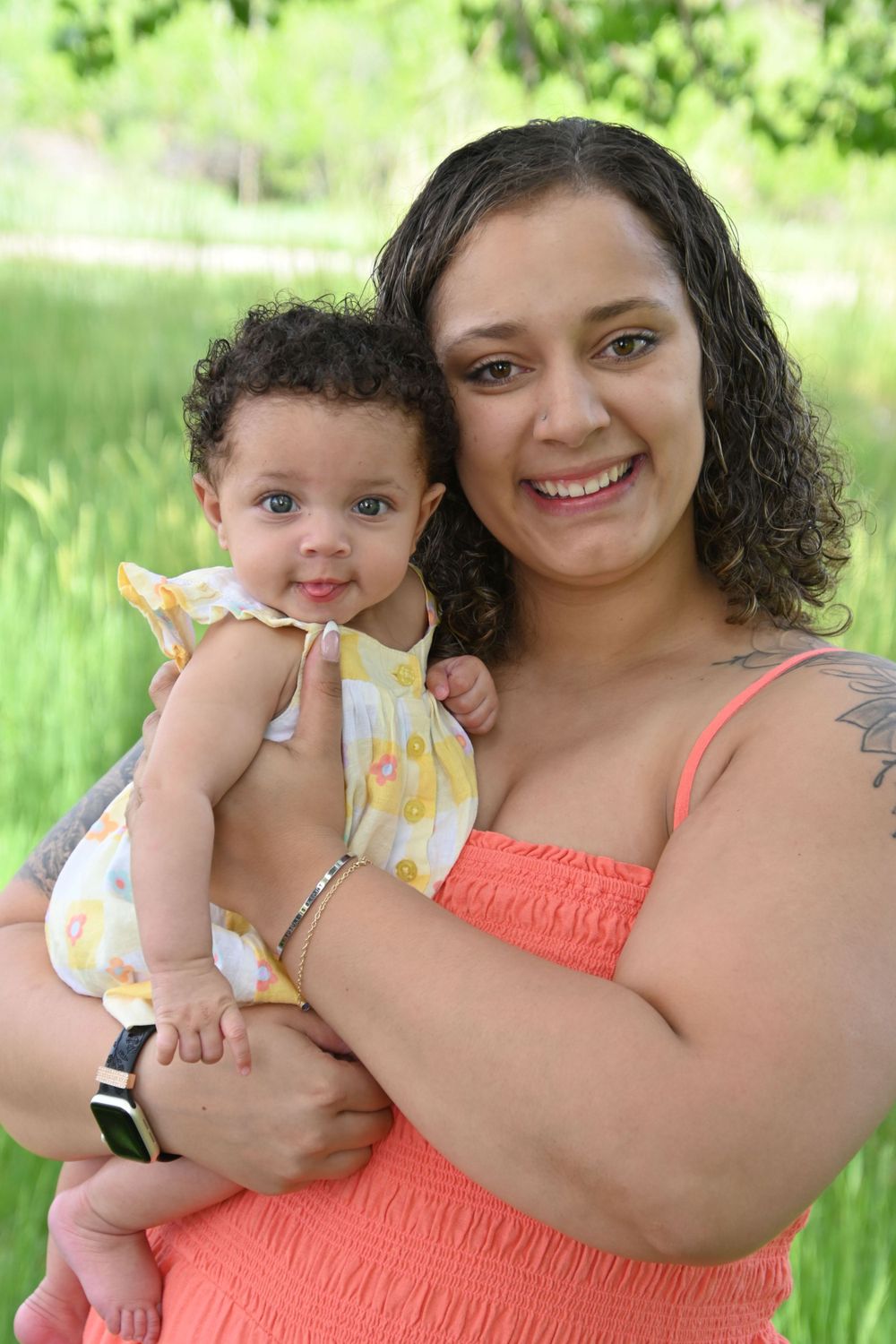 A parent and baby in matching coral and yellow outfits pose for an outdoor portrait in a green field.