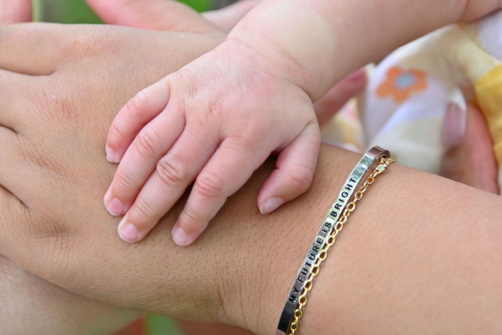 Close up of tiny baby hand resting on adult arm with silver bracelet.