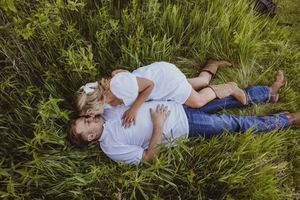 Couple lying together in tall green grass during summer photoshoot.