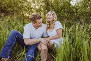 Couple sharing intimate moment while sitting in tall grass during golden hour.