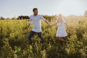 Couple running through a sunlit meadow in casual white outfits.