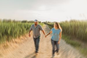 Couple walking hand in hand through a scenic path with tall grass at sunset.