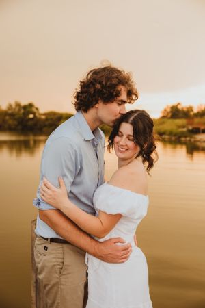Couple embracing during golden hour photoshoot by a lake.