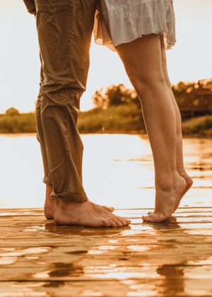 Bare feet of a couple standing together on wet surface during sunset.
