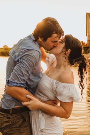Romantic couple embraces at sunset by the water in an intimate photoshoot series.