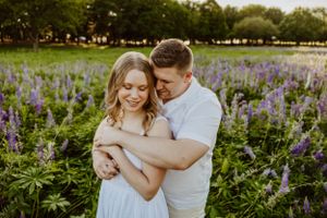 Couple embracing in field of purple wildflowers during sunset photo session.