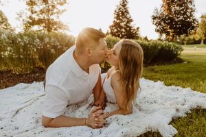 Couple laying on white blanket outdoors during golden hour photoshoot.