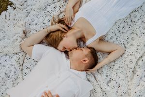 Intimate couple portrait session on white lace blanket in natural setting.