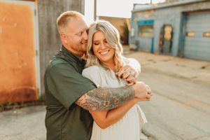 Romantic couple portraits against rustic industrial buildings at golden hour.