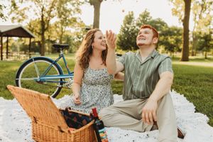 Couple enjoying a romantic picnic in a park with a wicker basket and blanket on a sunny day.