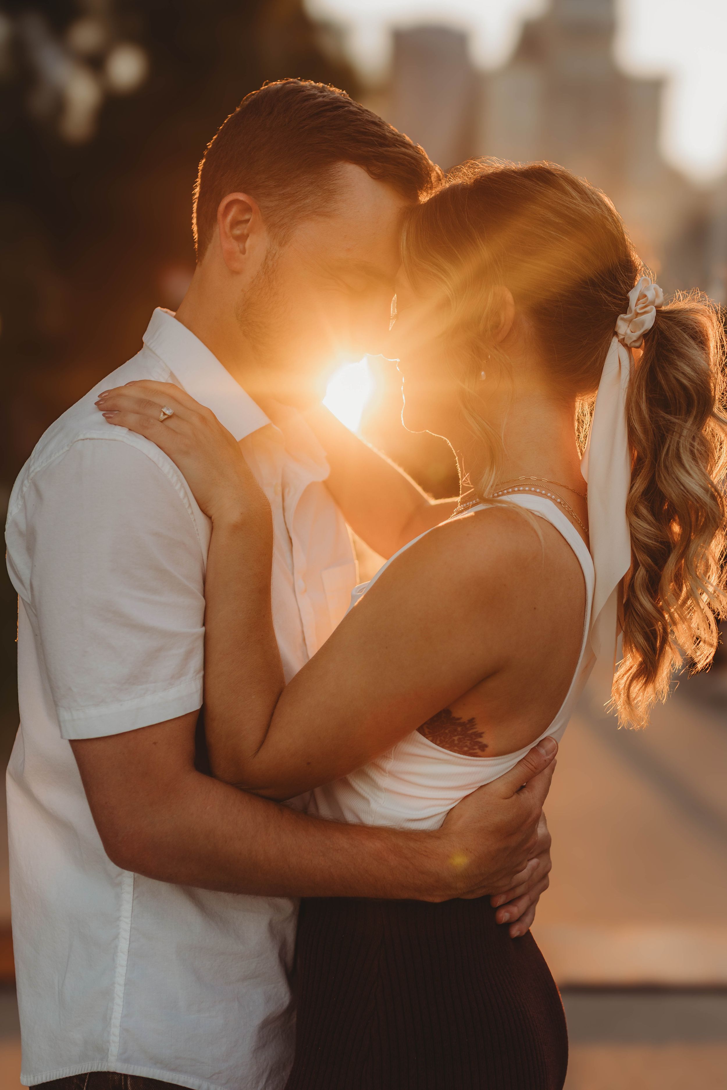 Couple embracing in golden sunset light with urban backdrop and lens flare.
