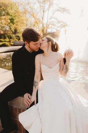 Romantic wedding photoshoot with couple in white dress and black suit against sunlit backdrop.