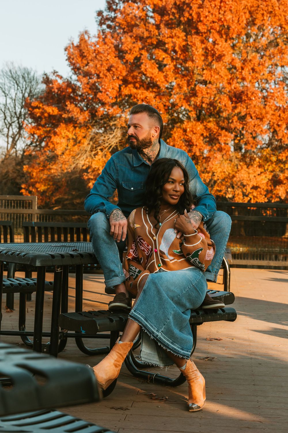 Couple sitting together on bench during autumn with vibrant orange fall foliage behind them.