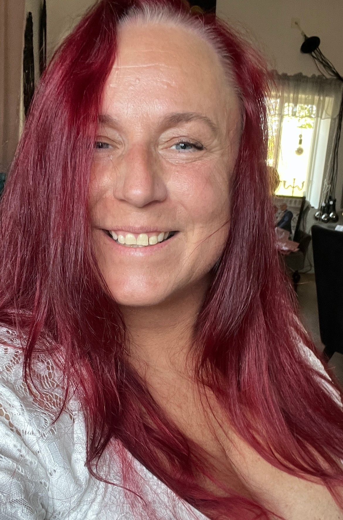 A person with vibrant red hair wearing glasses and a black shirt smiles warmly at the camera.Boudoir By Jane - Photo By Jane Svensson