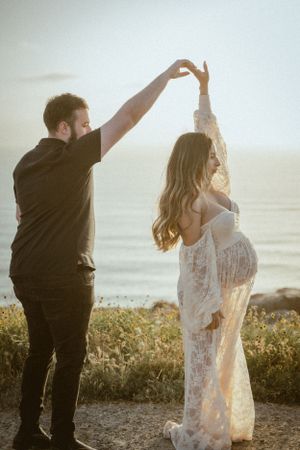 A couple dancing together at sunset, with the pregnant woman wearing a flowing lace dress.